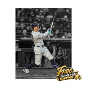 May include: A baseball player in a white pinstriped uniform with a dark helmet and blue socks swings a black bat. The player wears dark eye black under the eyes. A signature is visible on the right side of the black and white photograph.