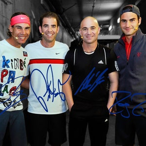 May include: Four men wearing athletic wear, including a white shirt with colorful text, a white shirt with a black and red stripe, a black shirt with a white logo, and a gray sweatshirt with a red stripe. The men are standing in a tunnel and have signed their names in blue ink on their shirts.