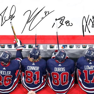 May include: Four hockey players wearing blue and red jerseys with their names and numbers on the back. The players are leaning over a red and white barrier. The players' names are Wheeler 26, Connor 81, Dubois 80, and Lowry 17.
