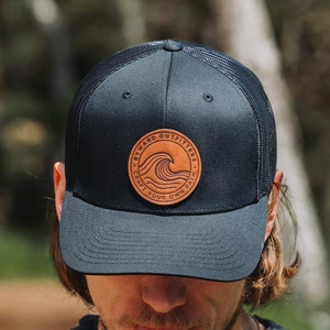 May include: A black and brown mesh trucker hat with a leather patch that says "Byward Outfitters - Craft Your Own Path" and a wave design.