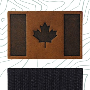 Peut inclure: Un écusson en cuir marron avec le drapeau canadien et le texte "Velcro Hook Backing" sur une bande de fermeture velcro noire.