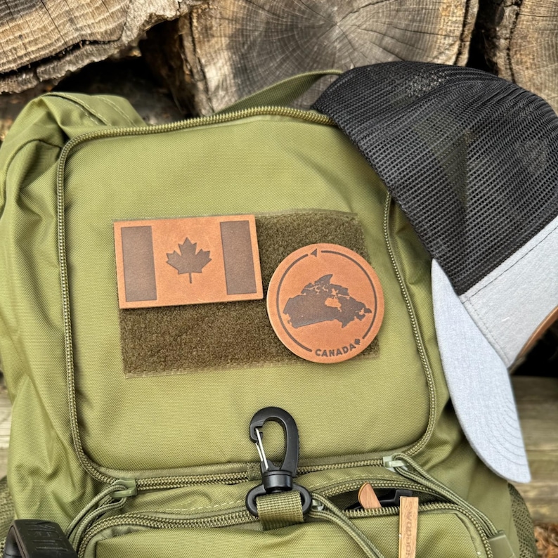 May include: A green backpack with two leather patches. One patch features a Canadian flag and the other patch features an outline of Canada with the word "CANADA" underneath.