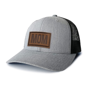 May include: A grey and black trucker hat with a brown leather patch that says "MOM" on it.