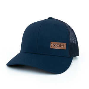 May include: A navy blue trucker hat with a brown leather patch that says "MOM" on it.