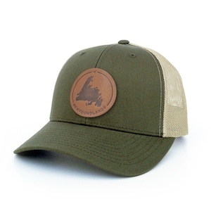 Peut inclure: Un chapeau de camionneur vert et beige avec un patch en cuir brun représentant le contour de Terre-Neuve et le texte "NEWFOUNDLAND".