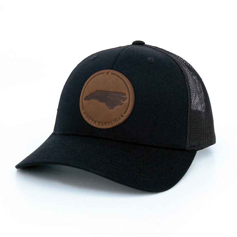 May include: Black trucker hat with a brown leather patch featuring the outline of North Carolina and the text "NORTH CAROLINA".