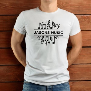 Op de afbeelding: Wit T-shirt met zwarte muzieknoten en de tekst "JASON'S MUSIC" gedrukt op de voorkant.