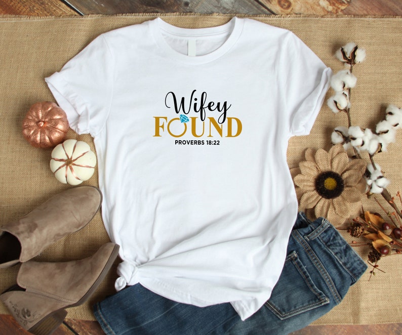 May include: White t-shirt with the text "Wifey Found" in gold lettering with a diamond graphic above the word "Found". The text "Proverbs 18:22" is printed below the main text.