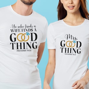 May include: Two white t-shirts with black text and a graphic of two gold rings with a blue diamond. The text on the first shirt reads "He who finds a WIFE FINDS A GOOD THING PROVERBS 18:22". The text on the second shirt reads "Mrs. GOOD THING PROVERBS 18:22".