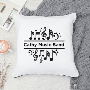 Op de afbeelding: Een wit kussen met zwarte muzieknoten en de tekst "Cathy Music Band" erop gedrukt.