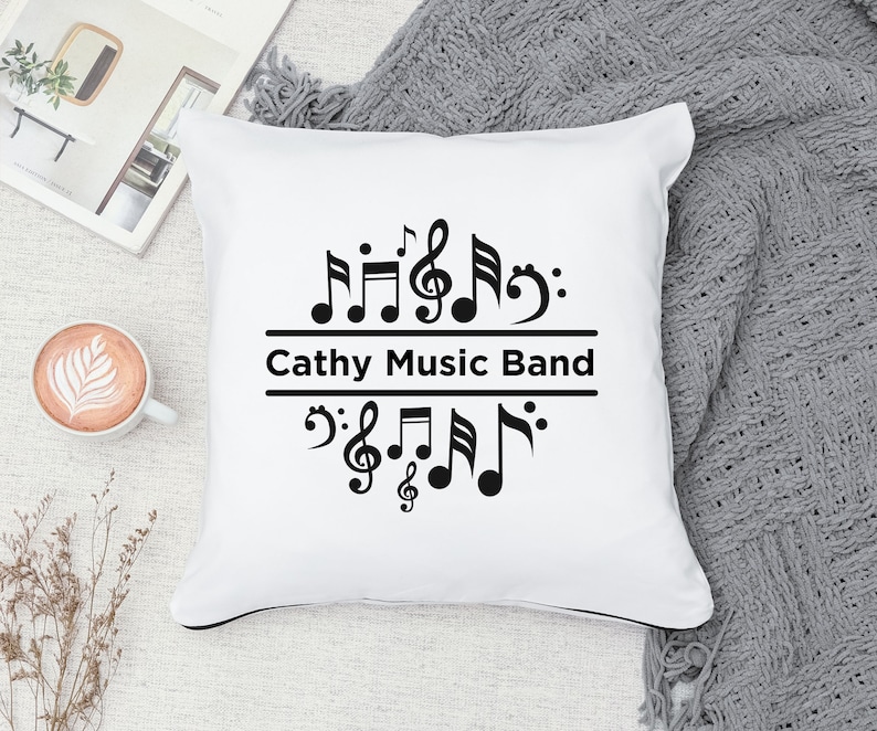 Op de afbeelding: Een wit kussen met zwarte muzieknoten en de tekst "Cathy Music Band" erop gedrukt.
