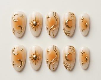 May include: A set of ten almond-shaped press-on nails featuring a gradient beige to tan base color. Each nail is decorated with raised gold-tone celestial motifs, including crescent moons, suns, wavy lines, and four-pointed stars in various sizes.