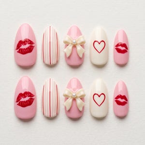 May include: A set of ten artificial nails in various designs. The nails feature pink, white, and cream colors with designs including red lips, a white bow with a pearl, red stripes, and a red heart.