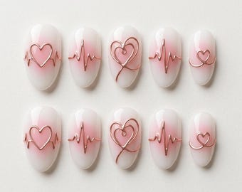 May include: A set of ten press-on nails featuring a soft pink and white gradient base. Each nail is adorned with raised rose gold metallic wire designs, including heart shapes and EKG heartbeat line patterns, arranged in two rows of five.