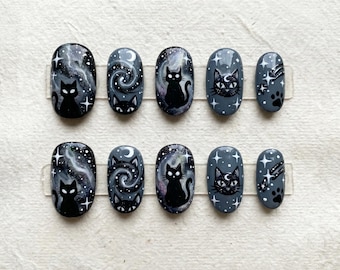 Könnte beinhalten: Set aus zehn künstlichen Nägeln mit dunkelgrauer Basis. Jeder Nagel hat ein einzigartiges Design, darunter schwarze Katzen-Silhouetten, Sternenhimmel, wirbelnde Galaxien und Pfotenabdrücke. Die Nägel sind oval geformt.