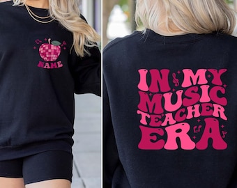 May include: Black sweatshirt with a pink apple graphic and the text "In My Music Teacher Era" on the back. The apple graphic has a disco ball design.