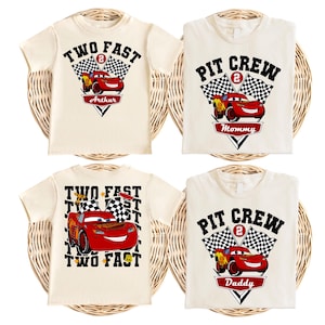 Op de afbeelding: Vier off-white t-shirts met rode raceauto-afbeeldingen, geblokte vlaggen en de tekst "TWO FAST" of "PIT CREW" met het cijfer 2. Twee shirts bevatten de namen "Arthur", "Mommy" of "Daddy" op rode banners onder de raceauto afgebeeld.