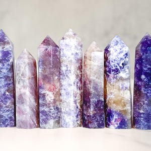 May include: Seven purple, white and blue crystal points arranged in a row. The points are all different sizes and shapes, and they have a variety of textures.