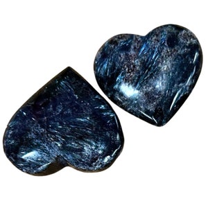 May include: Two heart-shaped stones in shades of blue and black with a shimmering, iridescent finish. The stones are made of kyanite, a crystal known for its calming and grounding properties.