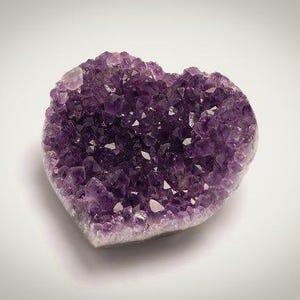 May include: A heart-shaped amethyst geode, showcasing a cluster of deep purple crystals. The crystals have a sparkling, crystalline structure, with a light-colored base. The geode is set against a white background.