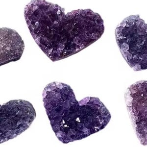 May include: Six heart-shaped amethyst crystal clusters in varying shades of purple and violet. The crystals have a rough, textured surface and are arranged against a white background. Each heart is approximately 2 inches wide.