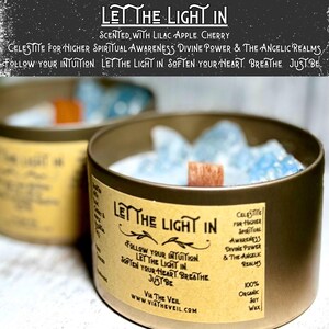 May include: Two gold candle jars with a light blue wax and a wooden wick. The label on the jar reads "Let the Light In" and "Celestite for Higher Spiritual Awareness Divine Power & The Angelic Realms". The label also reads "Follow your intuition. Let the light in. Soften your heart. Breathe. Just be." and "Via The Veil www.viatheveil.com".