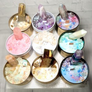 May include: Eight gold-rimmed glass candle jars with various colored wax and crystals inside. Each jar has a crystal sticking out of the wax. The crystals are clear, pink, purple, and blue.