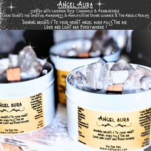 May include: Three white candle jars with clear quartz crystals inside. The jars have a yellow label with the text "Angel Aura" and the phrase "Shining brightly to your heart: Angel Aura fills the air. Love and light are everywhere!"