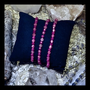 Pode incluir: Três fios de contas de pedras preciosas cor-de-rosa em um almofada de veludo azul escuro. As contas são redondas e têm uma aparência ligeiramente facetada.