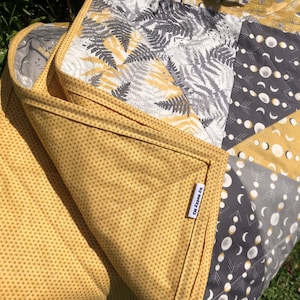 May include: A yellow and grey quilted play mat with a fern pattern on one side and a moon and arrow pattern on the other side. The mat has a label that says "The Cozy Co."