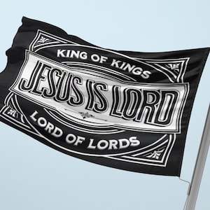 May include: Black flag with white text that reads "JESUS IS LORD" in a decorative frame. The flag also includes the phrases "KING OF KINGS" and "LORD OF LORDS". The flag is attached to a silver pole and is waving in the wind.