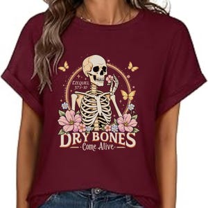 May include: Burgundy short-sleeved t-shirt featuring a skeleton holding a flower, surrounded by flowers and butterflies. The design includes the text "DRY BONES Come Alive" and the biblical reference Ezekiel 37:1-10.