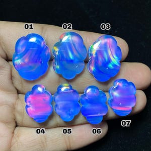 May include: Seven blue opal gemstones with a flower-like shape are displayed. Each stone has a unique pattern of internal colors, including pink, purple, and yellow, set against a blue background. The gemstones are numbered 01 through 07.