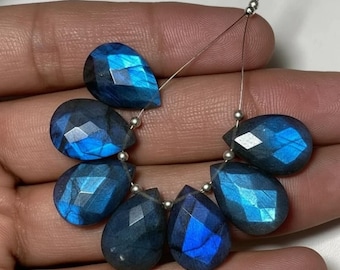 May include: A strand of faceted, teardrop-shaped labradorite beads. The beads are a deep blue with flashes of iridescent blue and silver. The beads are strung on a thin, silver-colored wire, and are ready for jewelry making.