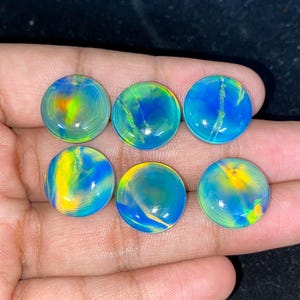 May include: Six round, polished opals with vibrant colors of blue, yellow, and green. The opals are displayed on a dark surface, showcasing their iridescent qualities. Each stone has a unique pattern.