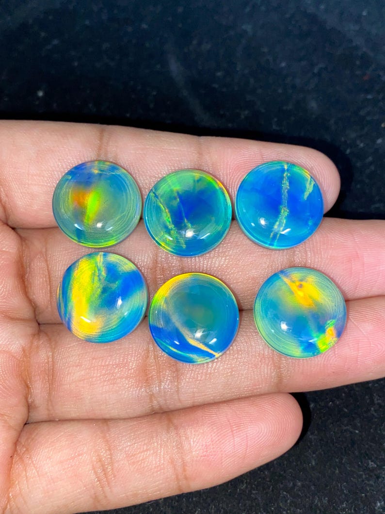 May include: Six round, polished opals with vibrant colors of blue, yellow, and green. The opals are displayed on a dark surface, showcasing their iridescent qualities. Each stone has a unique pattern.