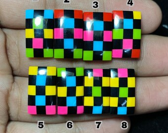 May include: Eight rectangular, colorful, checkerboard-patterned objects. Each object features a grid of black squares interspersed with vibrant colors like yellow, pink, green, red, and blue. The objects are held in a hand against a dark background.
