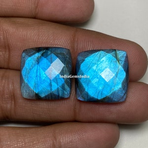 May include: Two square-shaped labradorite gemstones with a blue and green iridescent sheen. The stones are cut with a faceted design and have a smooth, polished finish.