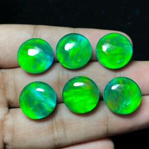 May include: Six round, polished gemstones with a vibrant green hue. The stones have internal color variations, with hints of blue and yellow. The gems are displayed against a dark background.