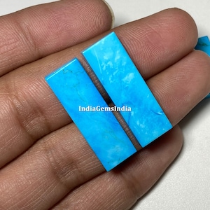 Puede incluir: Dos cabujones rectangulares de turquesa, cada uno mide aproximadamente 2,5 cm de largo y 1,25 cm de ancho. Los cabujones son de color azul claro con vetas blancas.