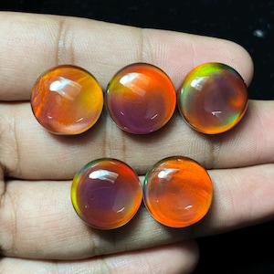 May include: Five round, polished gemstones with a vibrant colour gradient. The stones transition from orange to purple and green, with a glossy, reflective surface. The gemstones are displayed against a dark background.