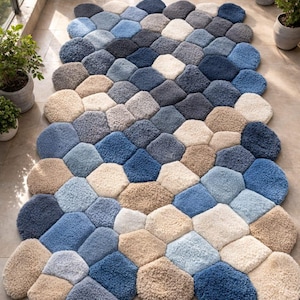 Puede incluir: Una alfombra grande y texturizada con un diseño único. La alfombra está compuesta por numerosas formas hexagonales en varios tonos de azul, beige y gris. La alfombra está colocada sobre un suelo embaldosado, con plantas en macetas al fondo.