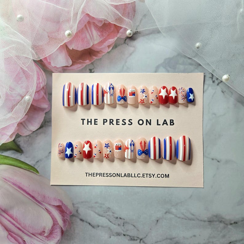 Pode incluir: Um conjunto de unhas posti&ccedil;as com tema patri&oacute;tico. As unhas apresentam listras vermelhas, brancas e azuis, estrelas e desenhos de la&ccedil;os. O texto "THE PRESS ON LAB" e "THEPRESSONLABLLC.ETSY.COM" est&aacute; impresso no cart&atilde;o.
