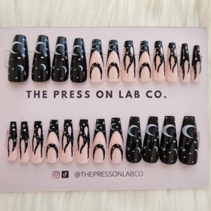 May include: A set of 10 press-on nails with a black and pink design. The nails feature a crescent moon and stars on a black background, and a flame design on a pink background. The nails are arranged on a pink card with the text "THE PRESS ON LAB CO."