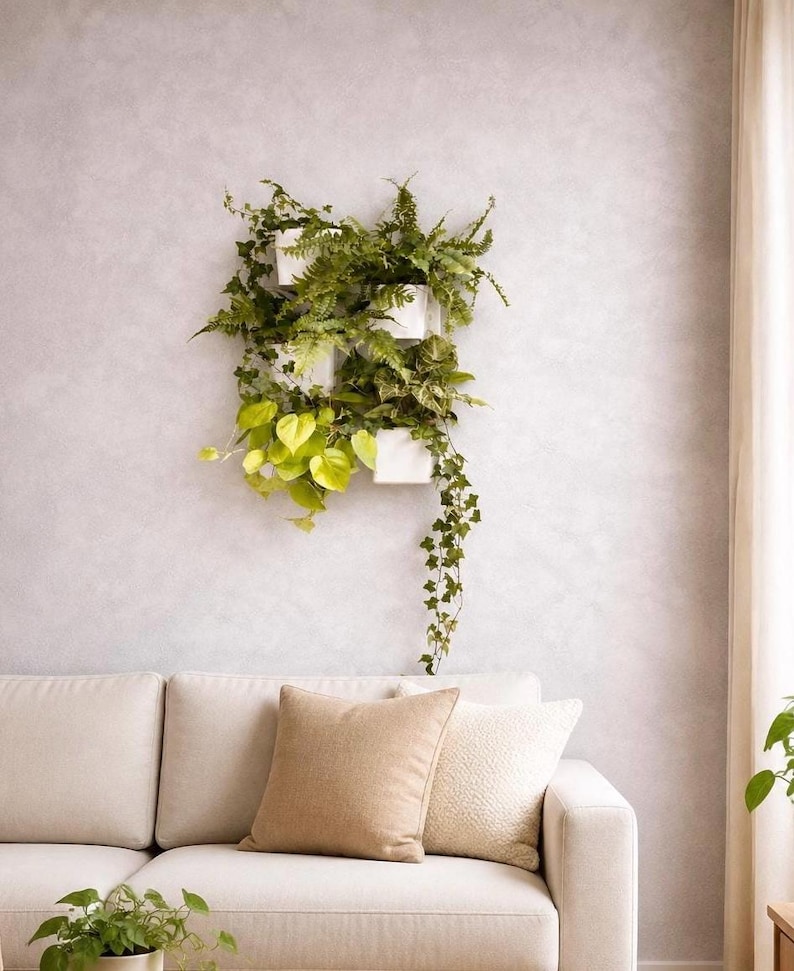 Vertikale Pflanzenwand mit weißen Pflanztöpfen, Farnen und rankenden Grünpflanzen über einer hellen Couch in einem modernen Wohnzimmer.