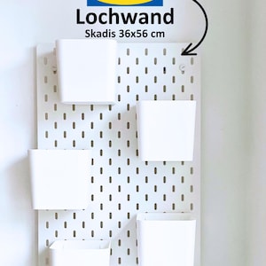 May include: White pegboard with the IKEA logo and the text "Lochwand Skadis 36x56 cm". Five white storage bins are attached to the pegboard.