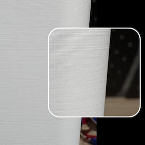May include: Close-up of a white, textured surface with a slightly curved edge. The surface has a subtle, horizontal pattern.