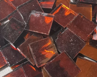May include: A pile of small, square, iridescent glass tiles in shades of amber and brown.