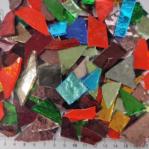 May include: A collection of colorful, iridescent glass pieces in various shapes and sizes. The glass pieces are arranged on a white surface with a ruler measuring 17 inches.