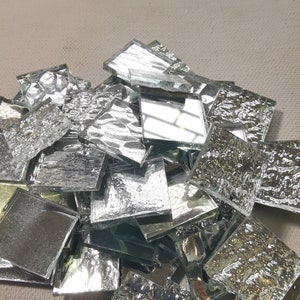 May include: A pile of silver-colored glass mosaic tiles with a textured surface. The tiles are irregular in shape and size.